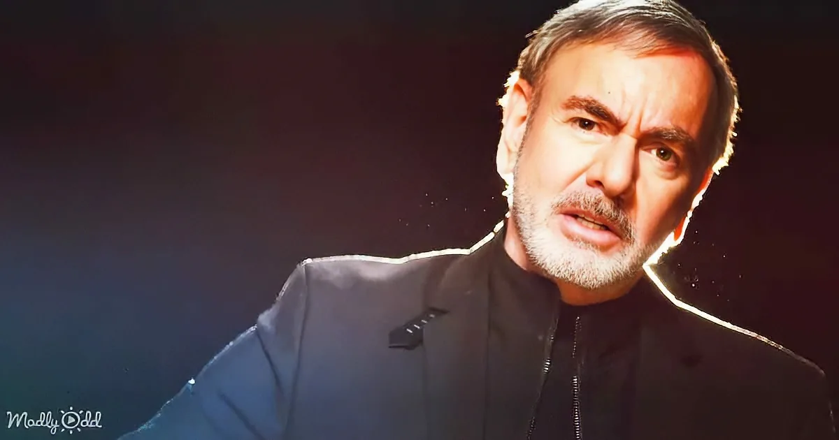 A man with short hair and a beard, wearing a dark jacket, is shown in a close-up with a dark background.