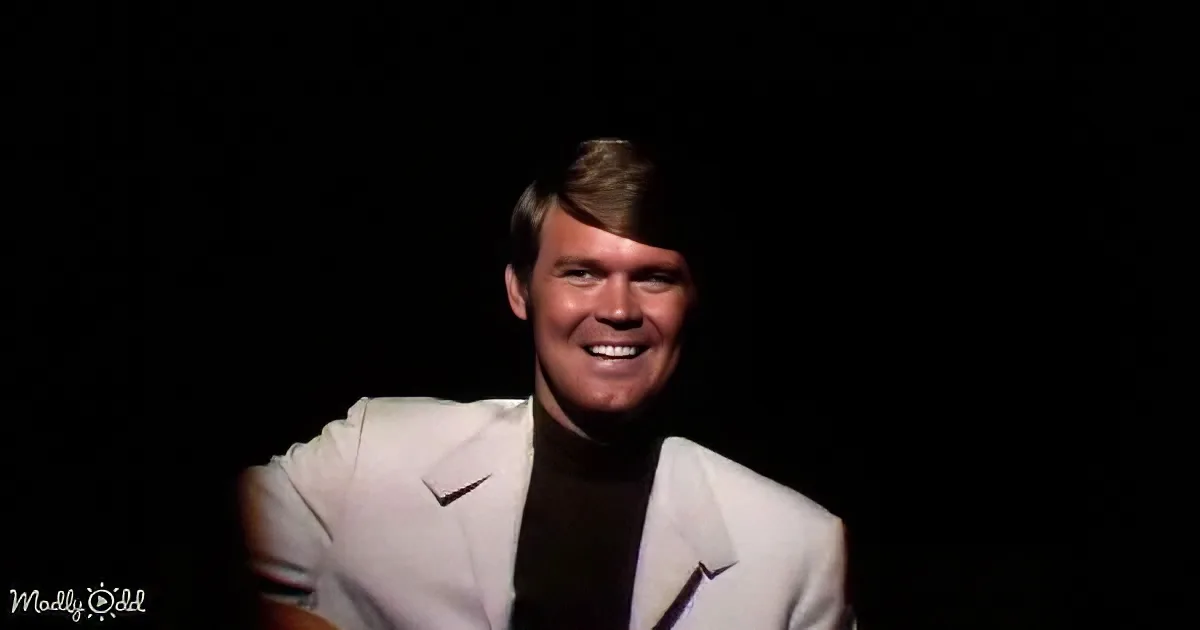 A man in a white suit smiles brightly against a dark background.