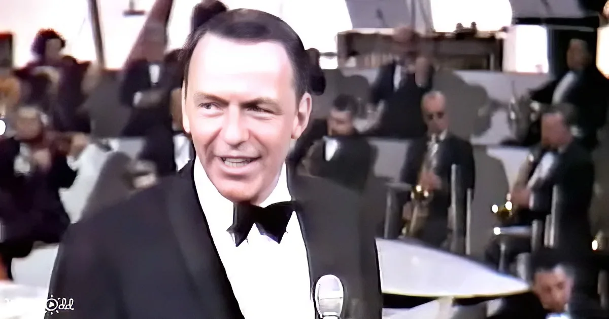 Frank Sinatra in a tuxedo smiles at a microphone, with an orchestra in the background.