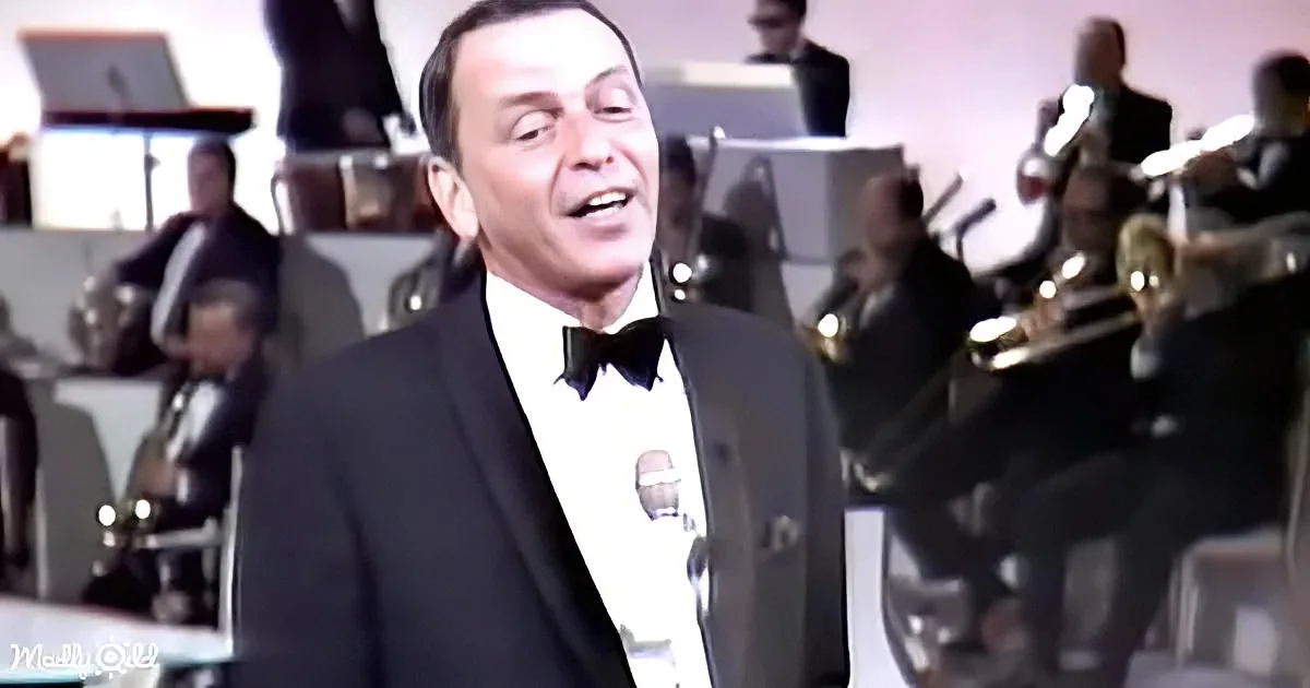 A man in a tuxedo sings into a microphone, with a band in the background.