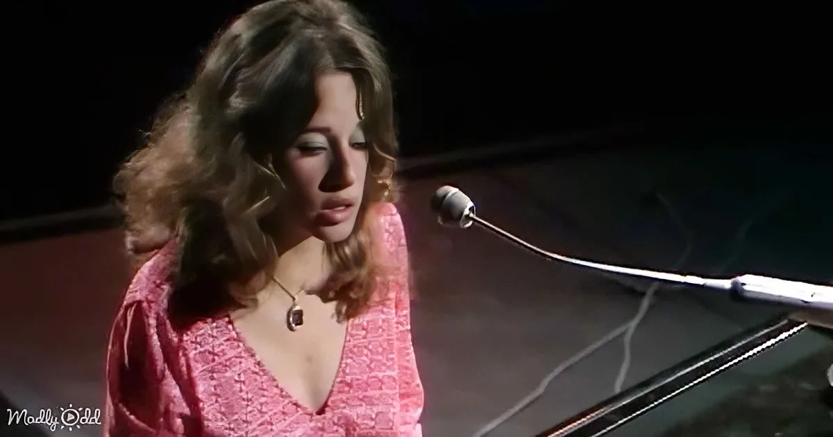 A woman in a pink dress sings into a microphone, her hair flowing, with a dark background.