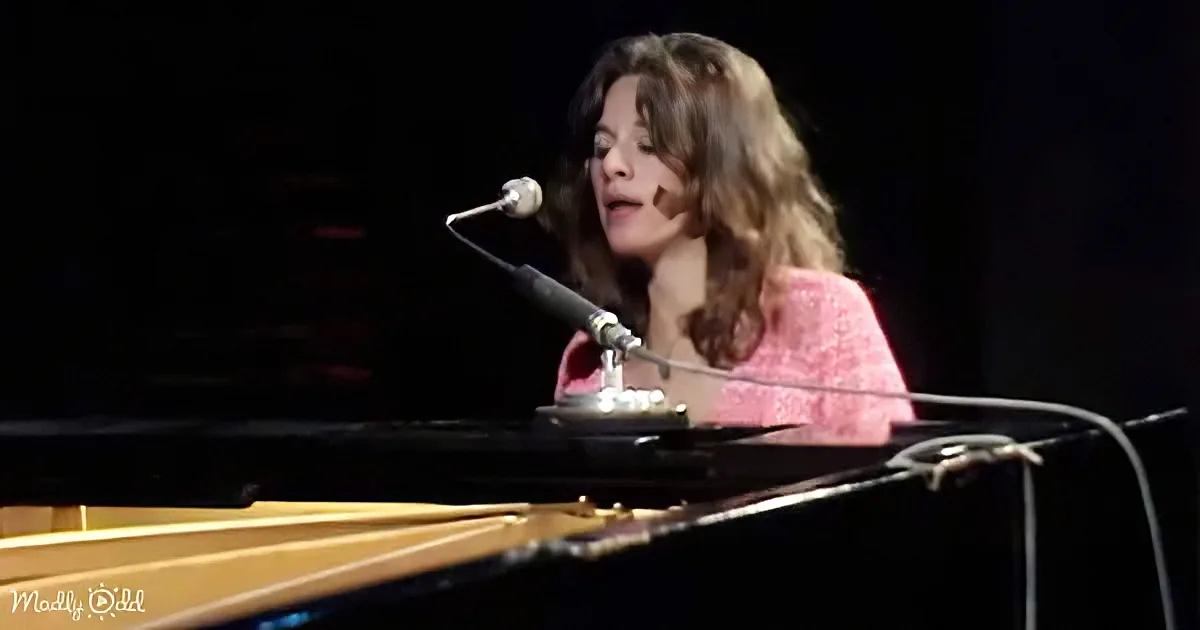 A woman in a pink top sings into a microphone while playing a piano.
