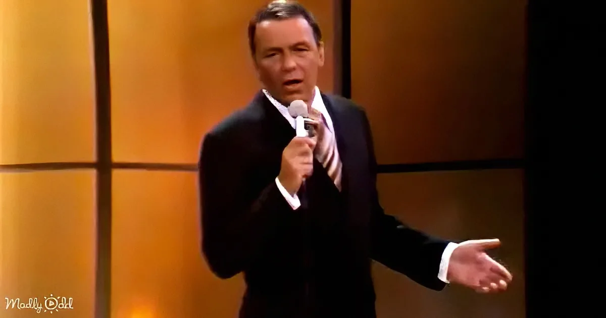 A man in a suit sings into a microphone, gesturing with his right hand.
