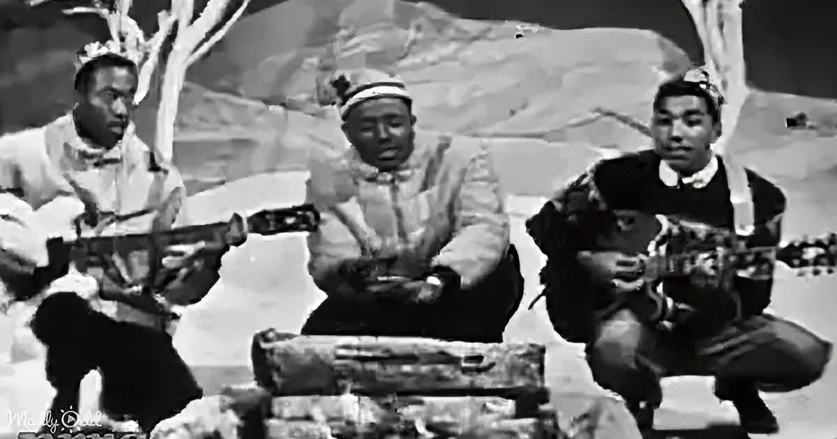 Three individuals in traditional attire play stringed instruments in a desert-like setting.