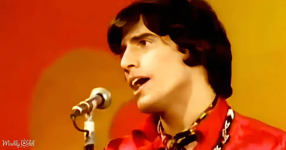 A person in a red outfit sings into a microphone against a red and yellow background.