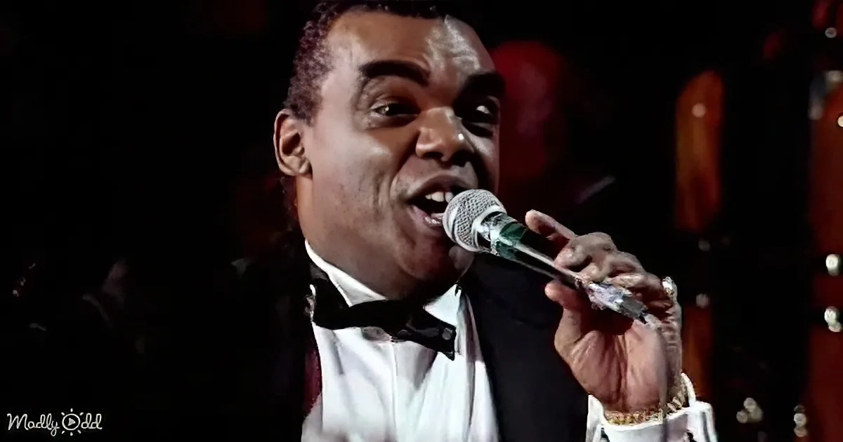 A man in a tuxedo sings passionately into a microphone, his expression intense.