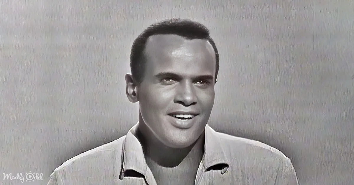 A man with short hair, wearing a light-colored collared shirt, smiles against a plain background.