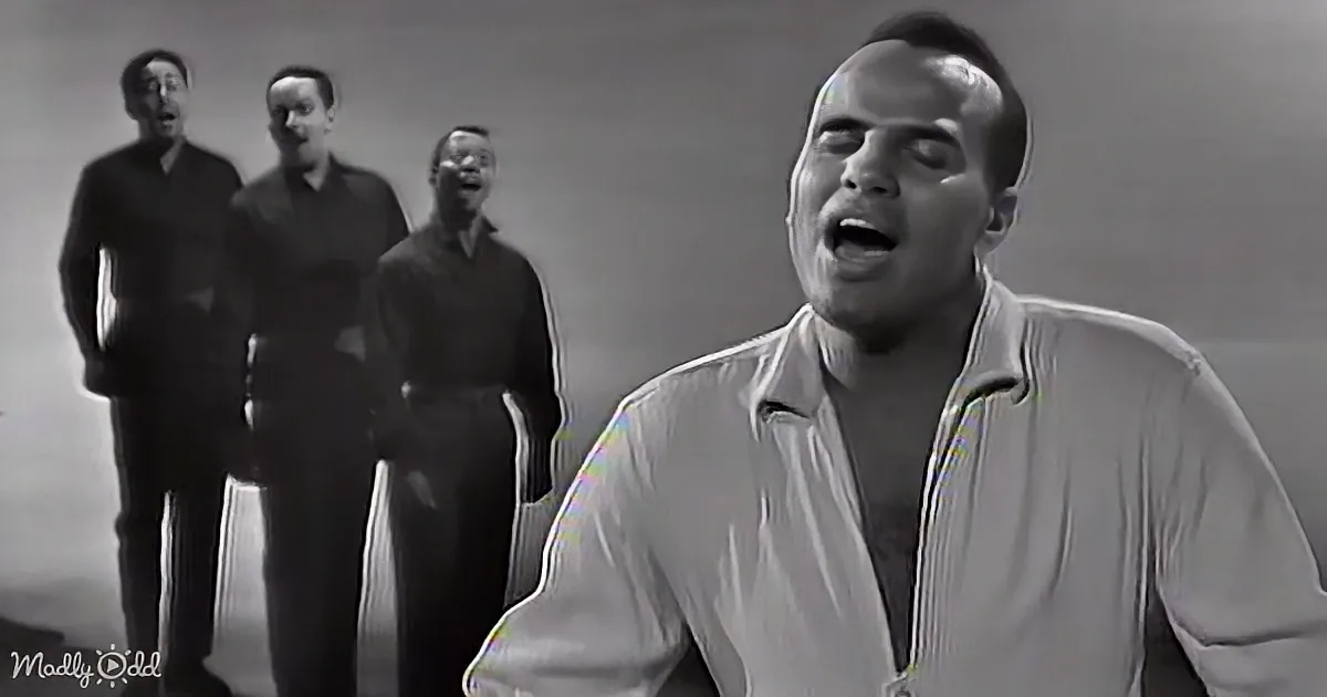 A man in a white shirt sings passionately in the foreground, with three other men in dark suits behind him.