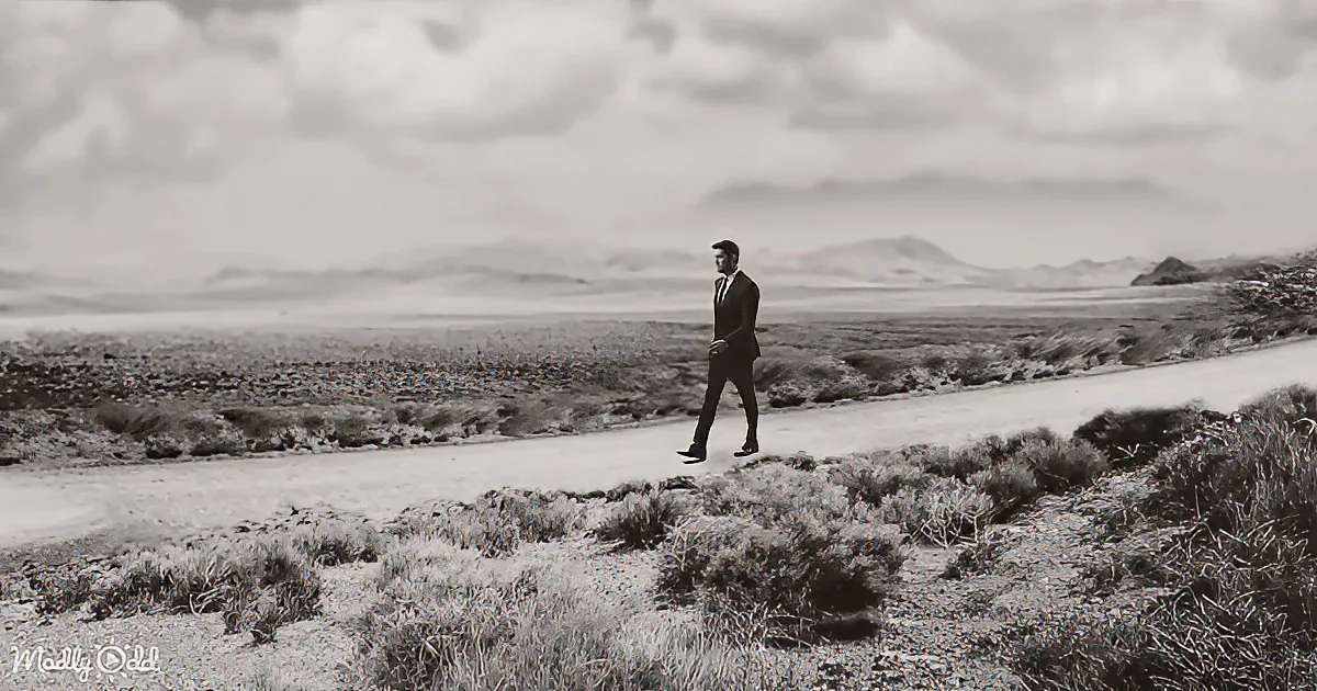 A man in a suit and hat is floating mid-air on a dirt road in a barren landscape.