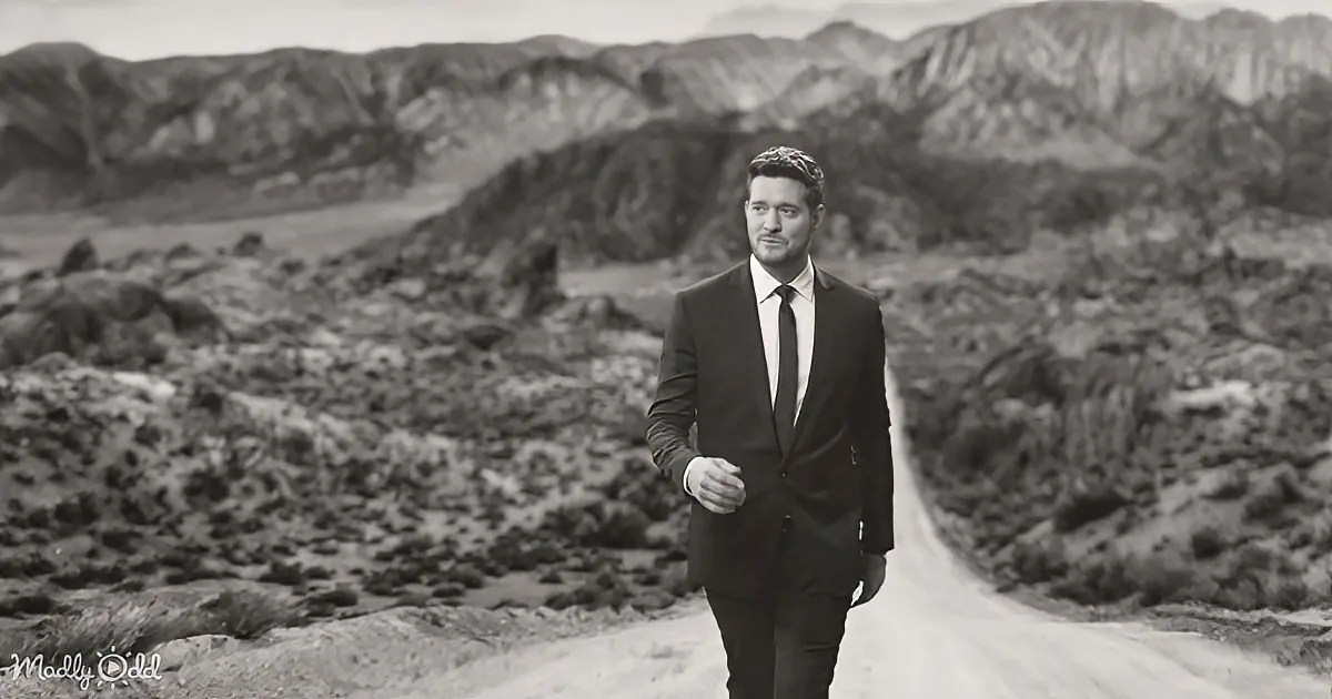 A man in a suit walks down a desert road, surrounded by rugged terrain.
