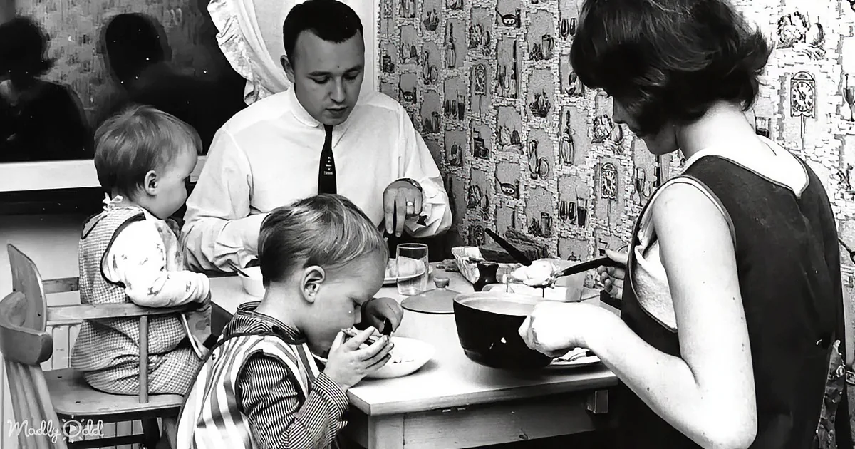 A family of four enjoys a meal together at a dining table, with a vintage wallpaper backdrop.