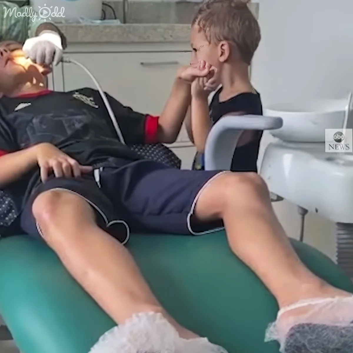 A young boy sits in a dental chair, appearing nervous, while a dentist examines his teeth.