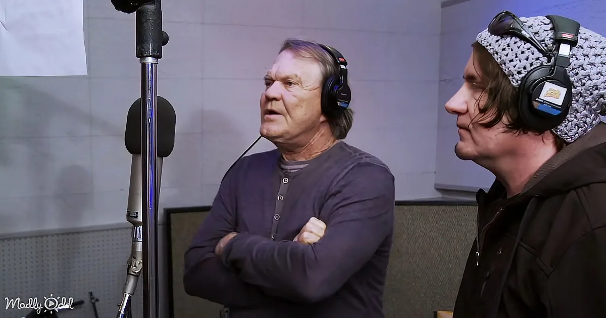 Two men in a recording studio, one with headphones and microphone, the other wearing a beanie and headphones.