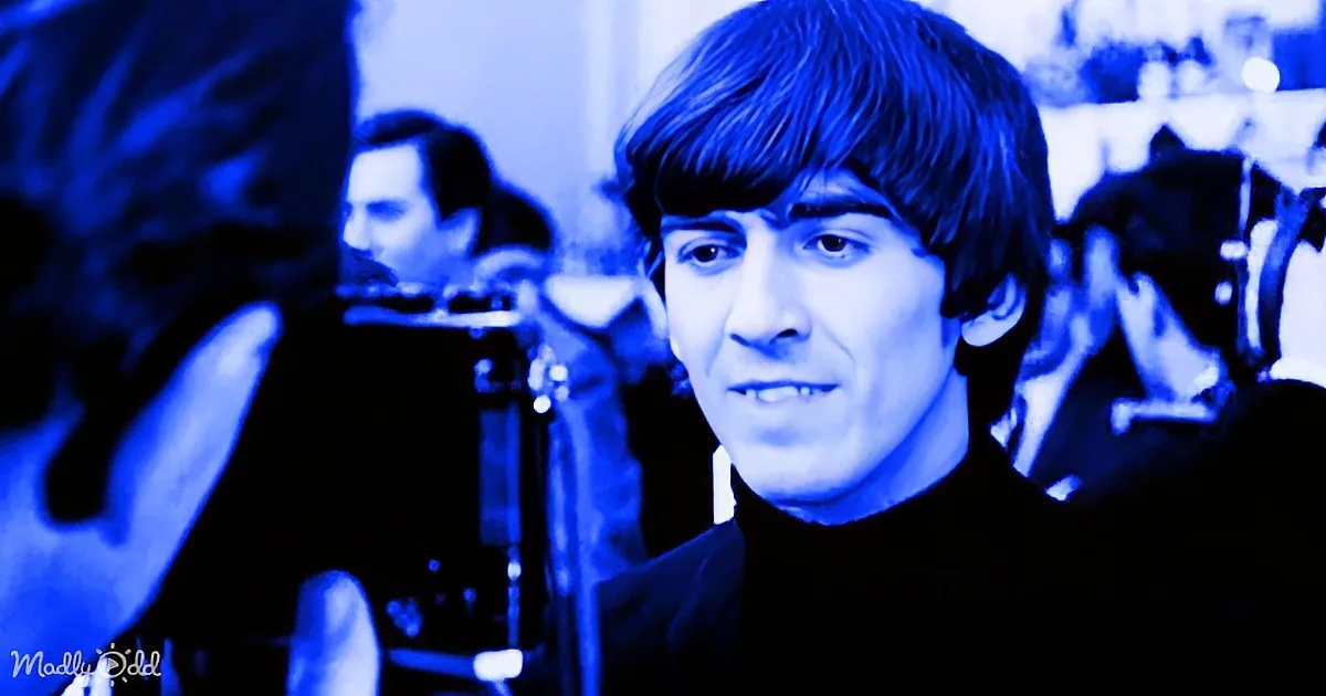 A man with dark hair and a black turtleneck stands in a blue-toned room, surrounded by blurred figures.