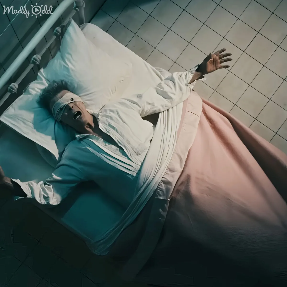 A person in a hospital bed, eyes blindfolded, mouth open, and arms outstretched, lying on a tiled floor.