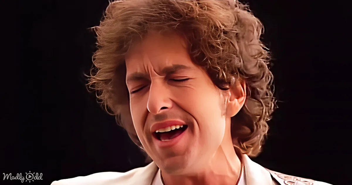 A person with curly hair and a white outfit is singing passionately with their eyes closed.