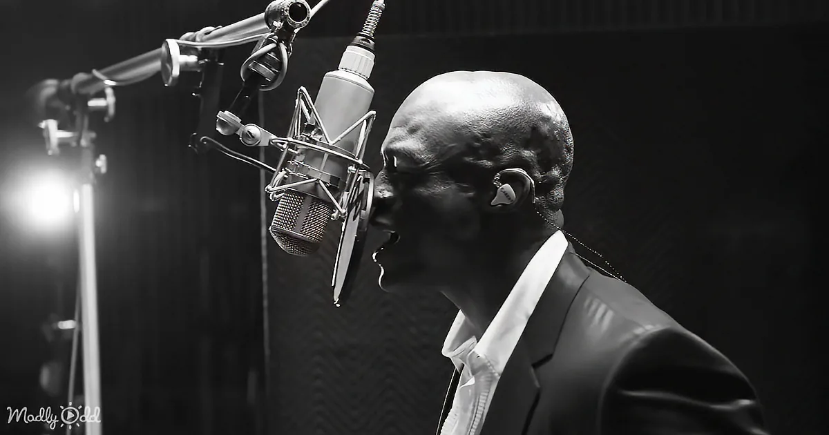 A man in a suit sings into a microphone in a recording studio.