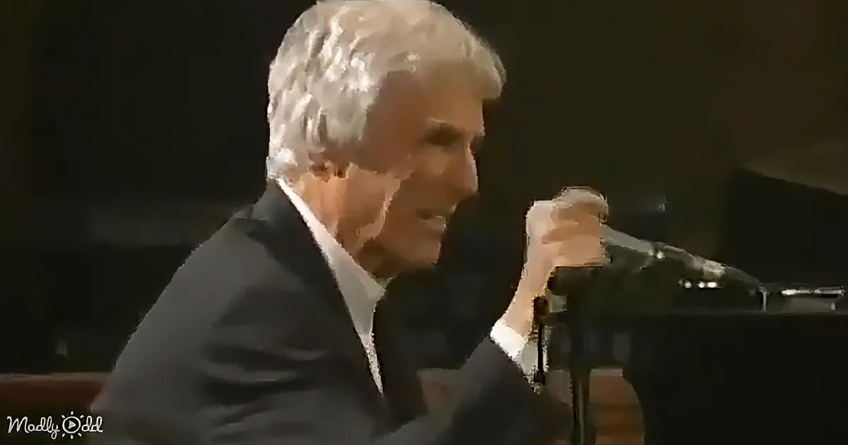 An older man in a suit sings into a microphone, holding it with his right hand.