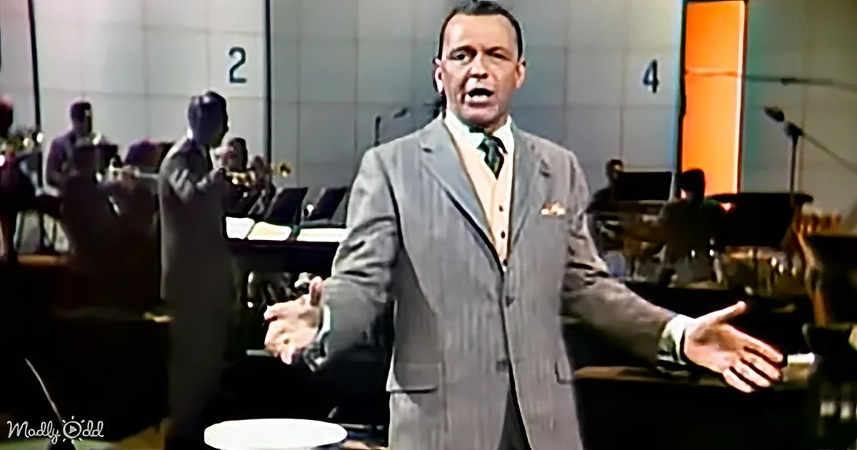 Frank Sinatra in a gray suit sings with a band in the background.