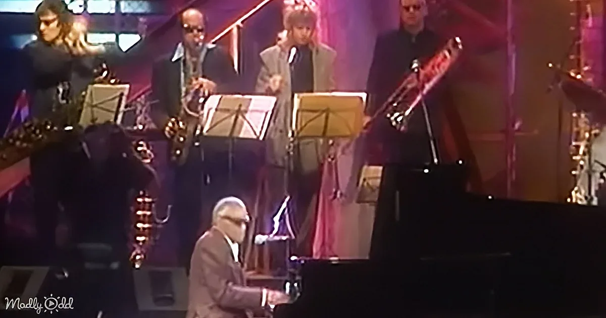 A man in a suit plays piano at a concert, surrounded by musicians with instruments.