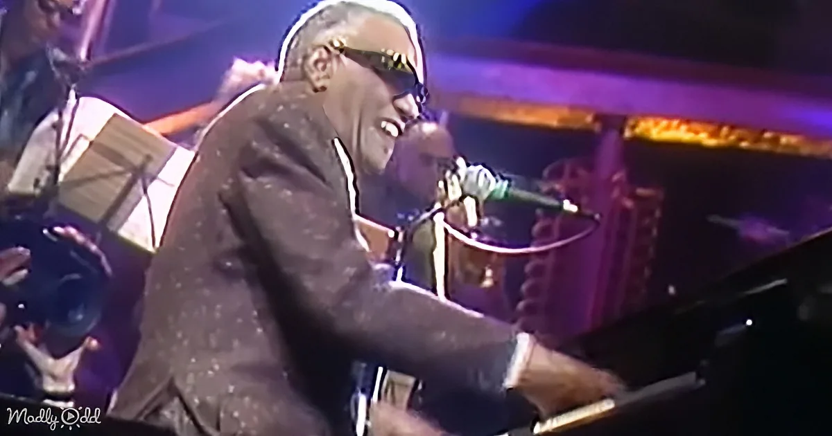 A man in a suit sings into a microphone while playing a piano on stage.