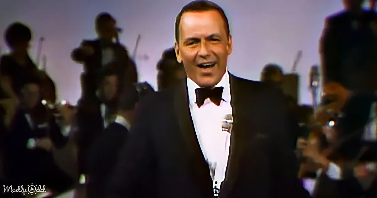 A man in a tuxedo sings into a microphone, with a band in the background.