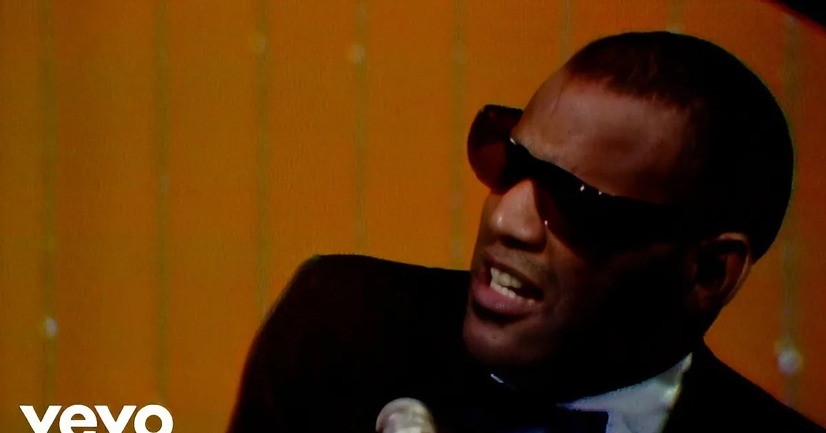 A man in a tuxedo and sunglasses sings into a microphone, wearing a bow tie.