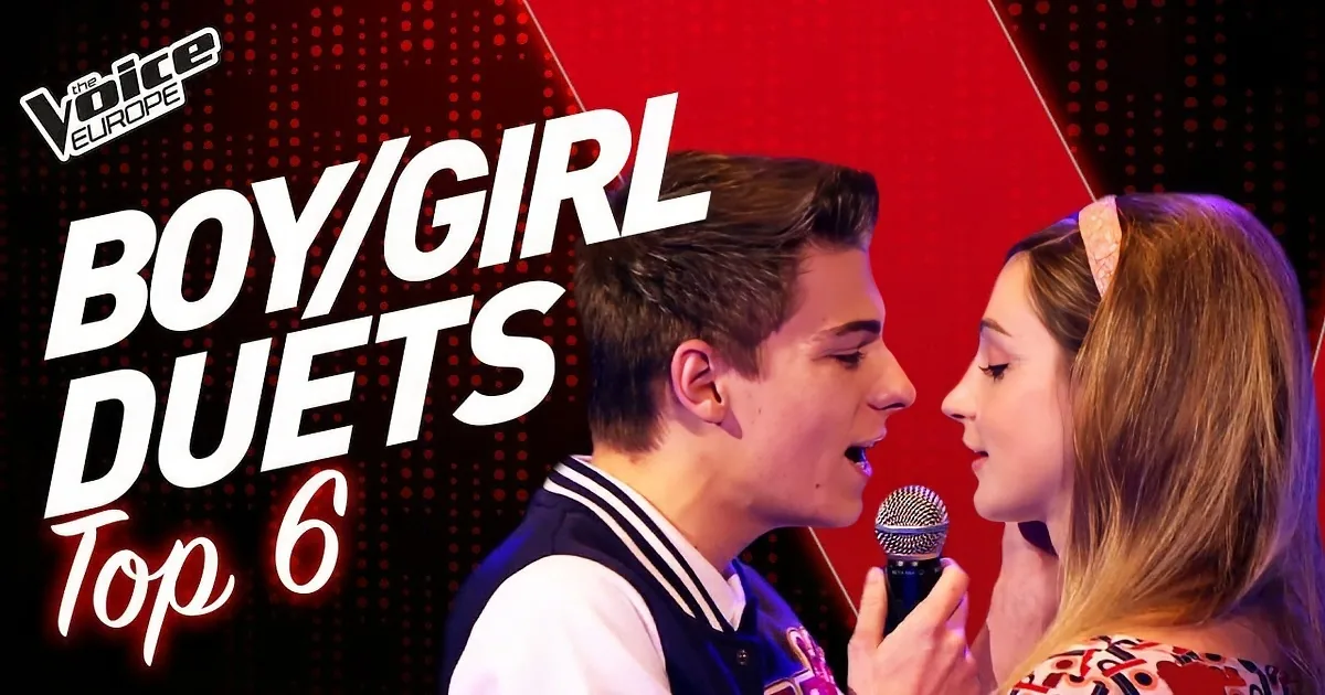A man and woman sing into microphones on stage, audience lights blurred in the background.