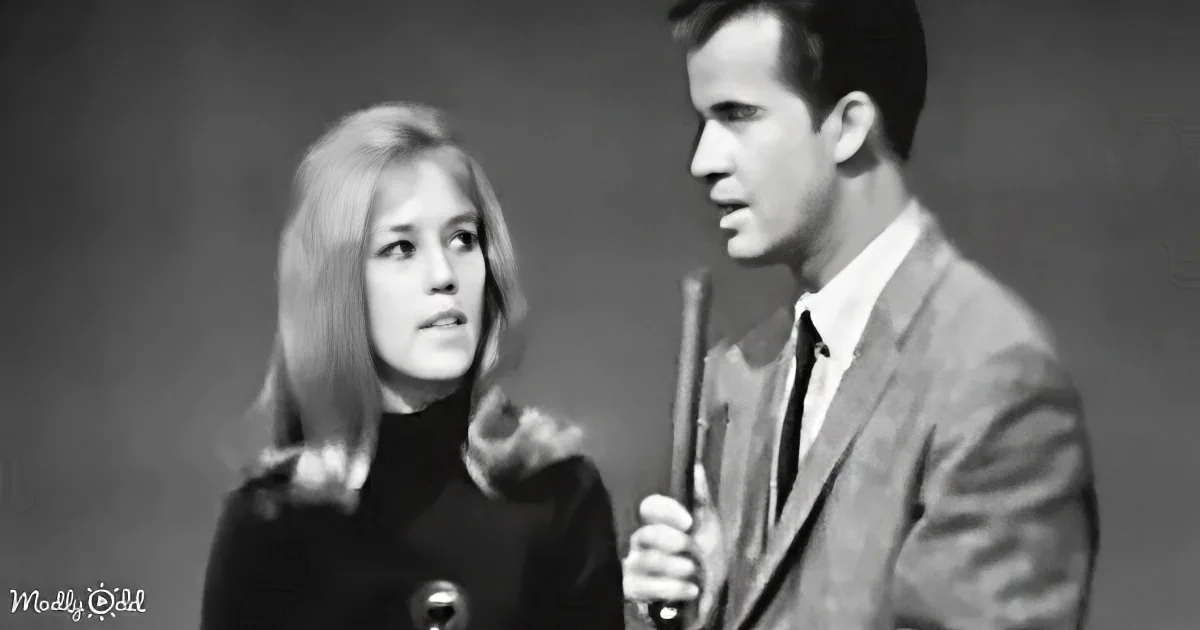 A man in a suit holds a microphone, speaking to a woman in a black top with a microphone in front of her.