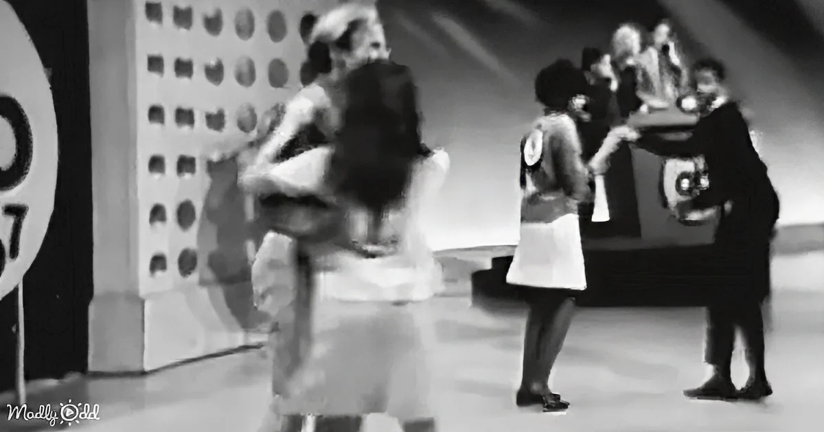 A woman in a white dress is being lifted by a man in a suit on a stage.