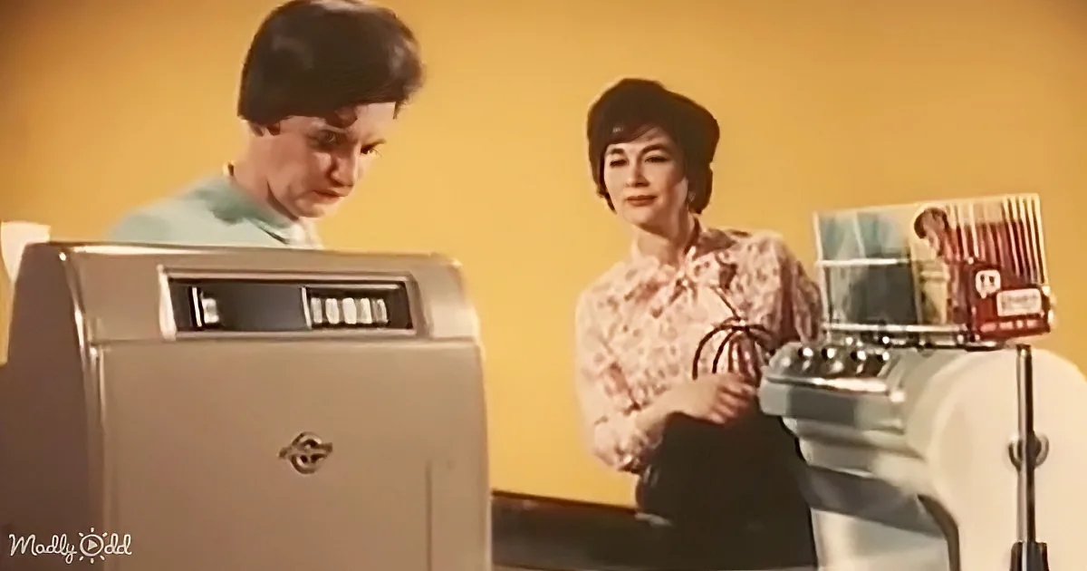 A woman in a floral blouse stands beside an old-fashioned cash register, with another person operating a similar machine...