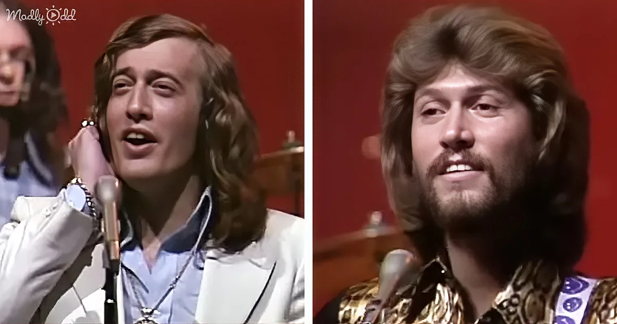 A man with long hair and a beard sings into a microphone, wearing a white suit and a gold shirt.
