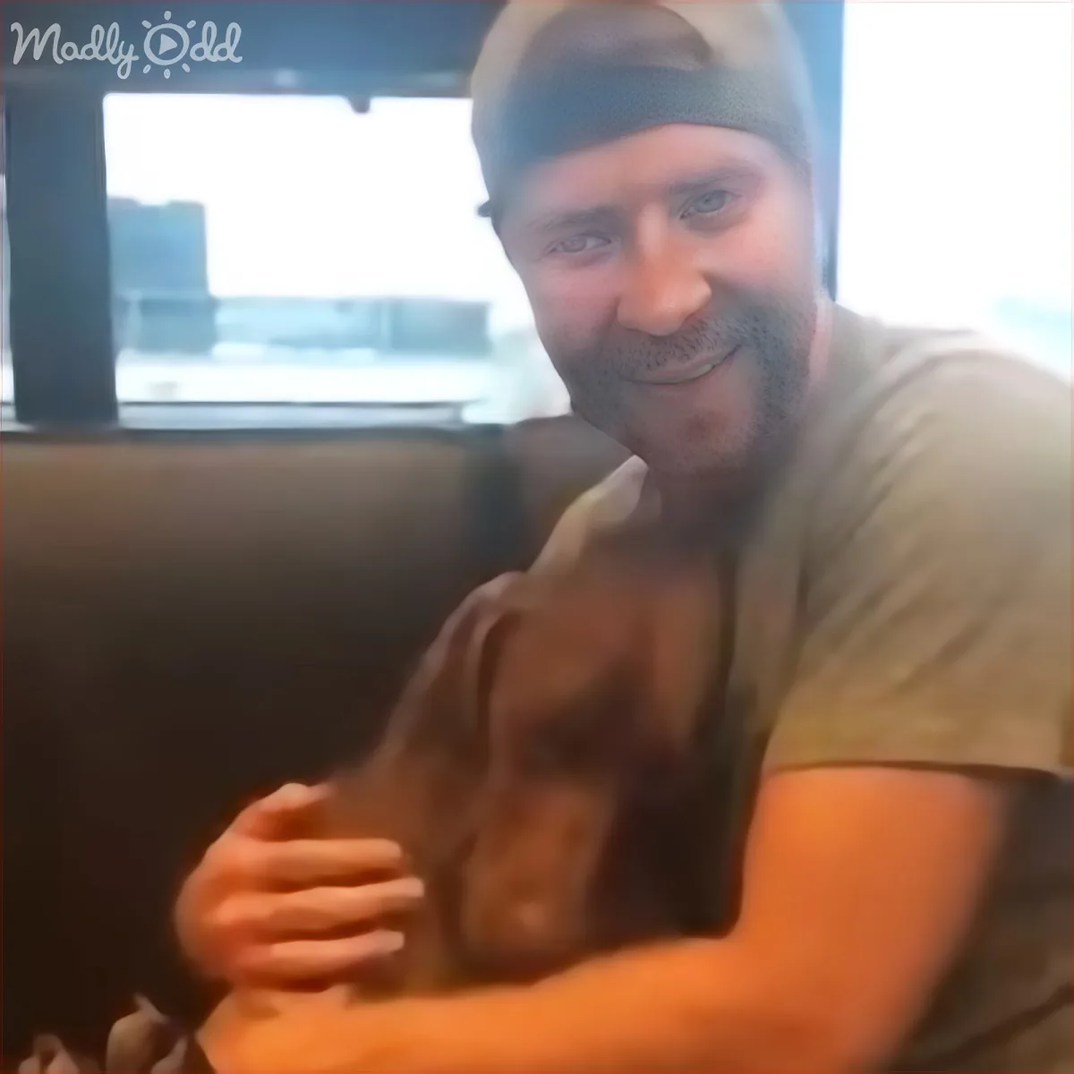 A man with a beard and a beanie is sitting on a couch, holding a small dog in his arms.