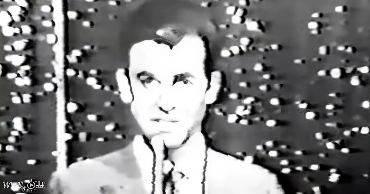A person in a suit and tie is standing in front of a patterned background.