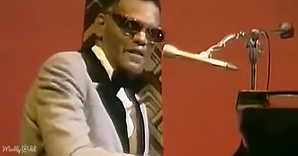 A man in a suit and sunglasses is playing a piano with a microphone in front of him.