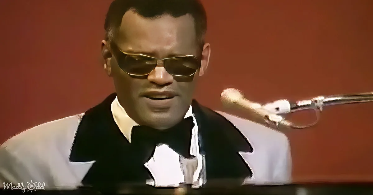 A man in a white shirt and black vest sings into a microphone, wearing sunglasses.
