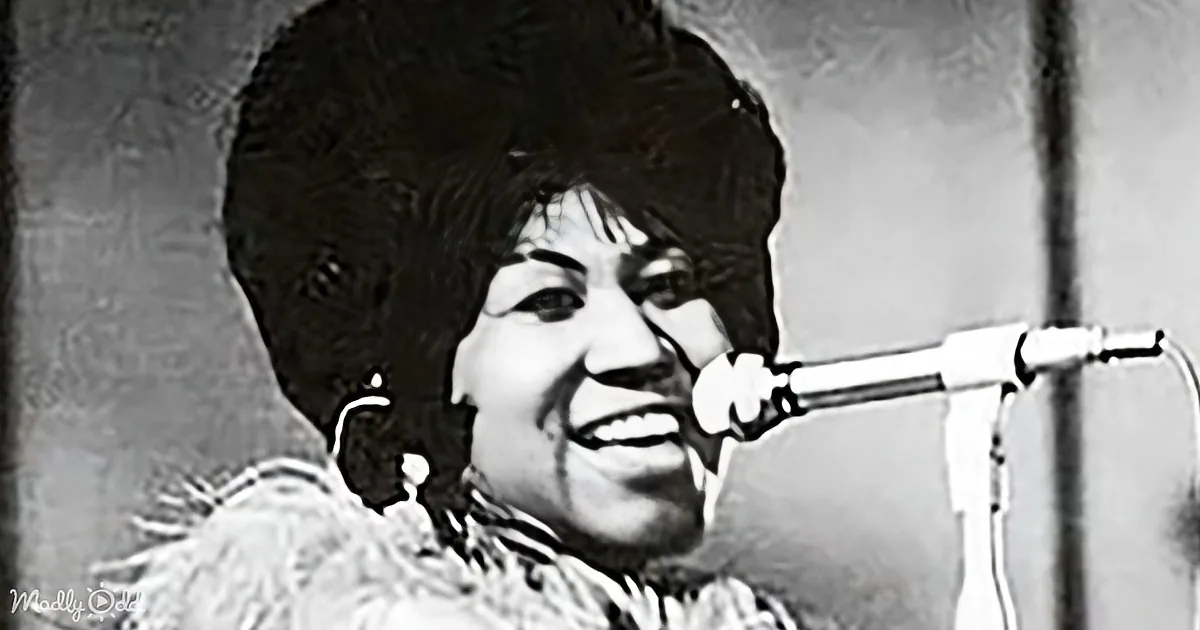 A smiling woman with a large afro hairstyle is singing into a microphone.