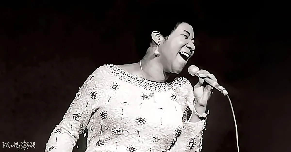 A woman in a beaded dress sings passionately into a microphone, her face illuminated by stage light.