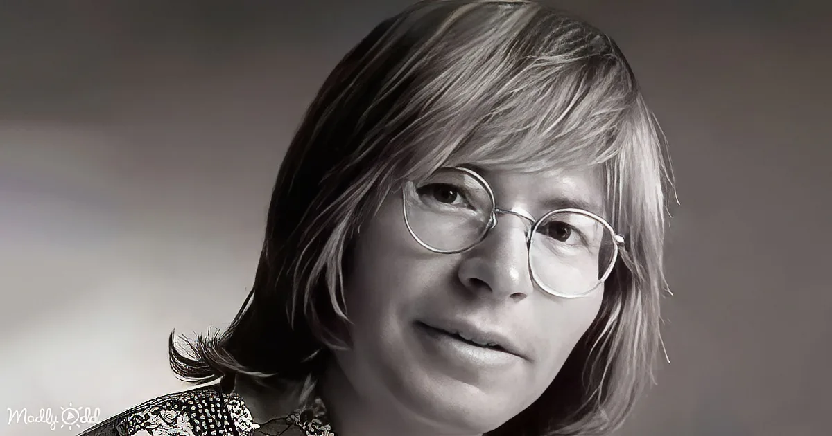 A person with shoulder-length hair and round glasses, wearing a patterned top, is shown in a close-up.