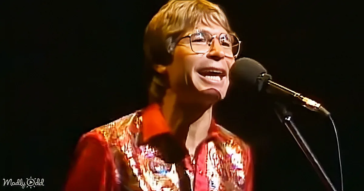 A person wearing glasses and a colorful shirt sings into a microphone on stage.