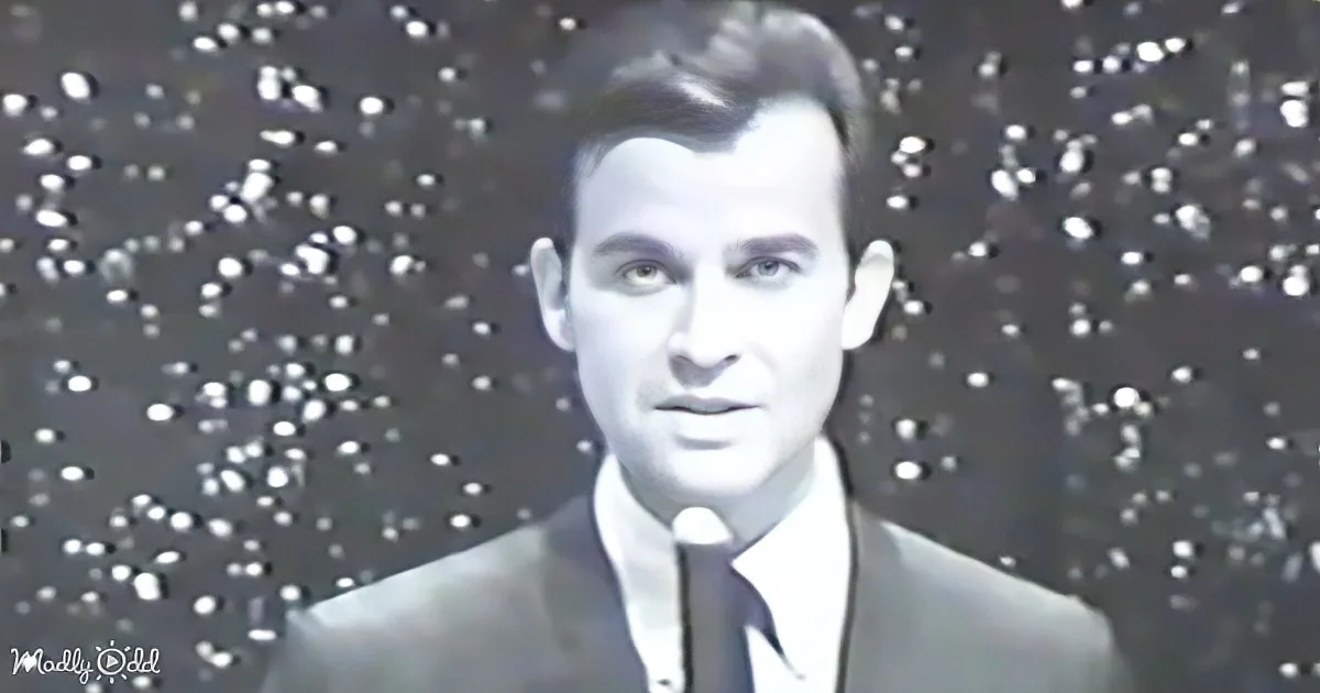 A man in a suit and tie stands in front of a perforated background.