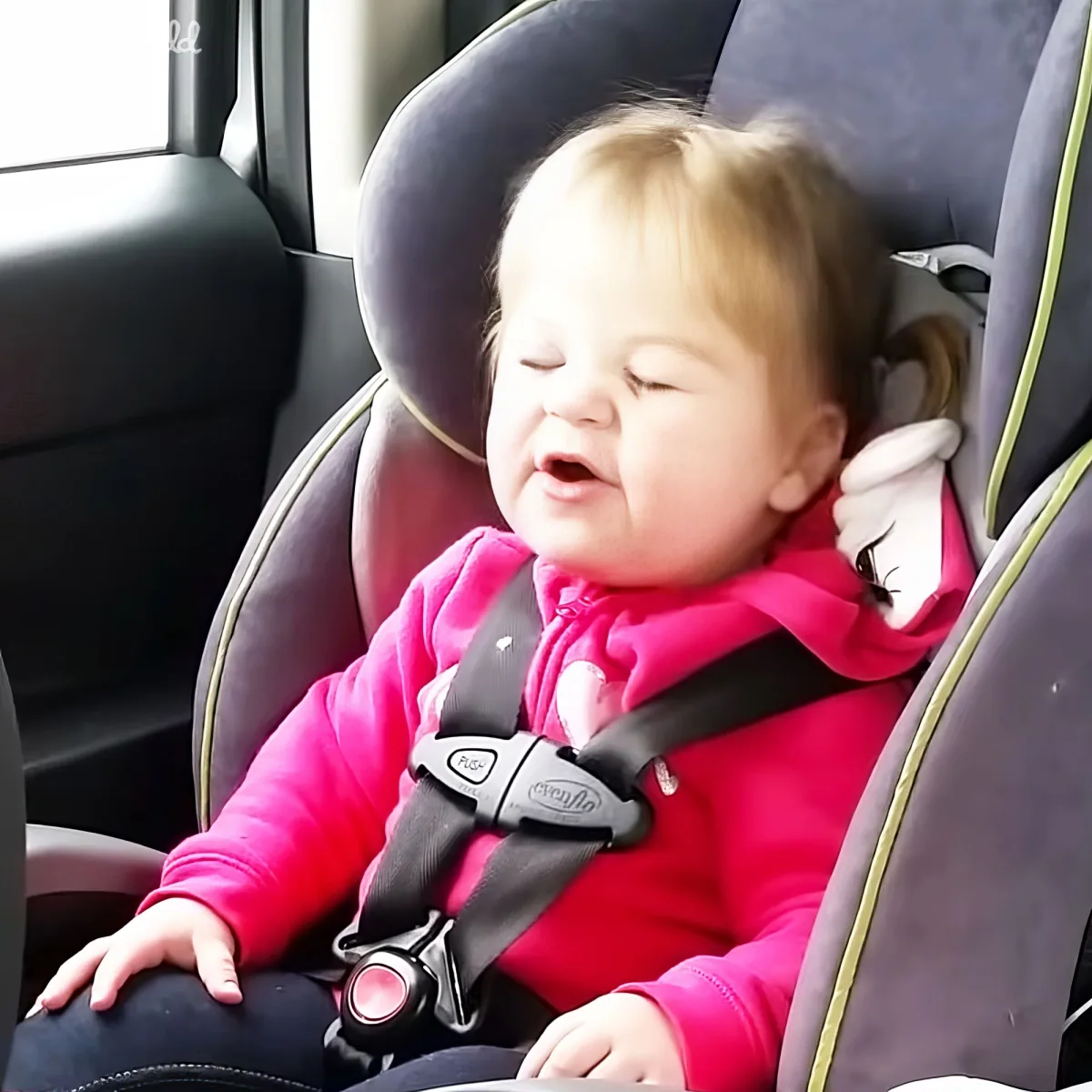 A baby in a pink hoodie sleeps peacefully in a car seat with a seatbelt.