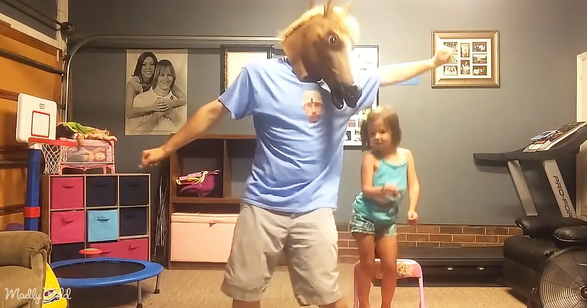 A man in a horse mask dances in a room with a child, surrounded by toys and exercise equipment.