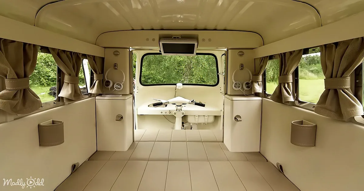 The interior of a van with a retro design, featuring a steering wheel, storage compartments, and large windows with curtains.