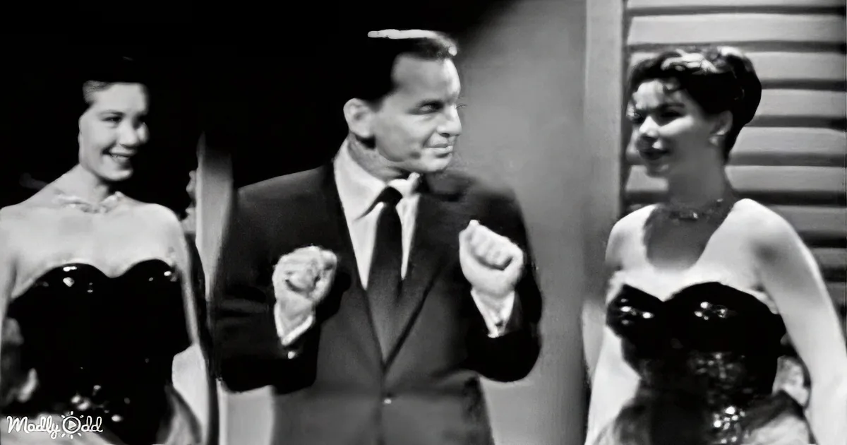 A man in a suit dances with two women in strapless dresses, all smiling.