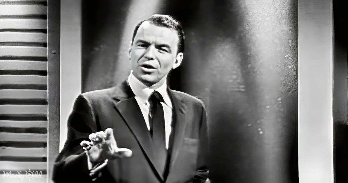 A man in a suit and tie gestures with his right hand, appearing to speak or present.