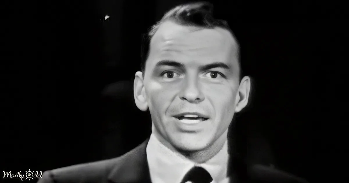 A man in a suit and tie, speaking into a microphone, with a dark background.