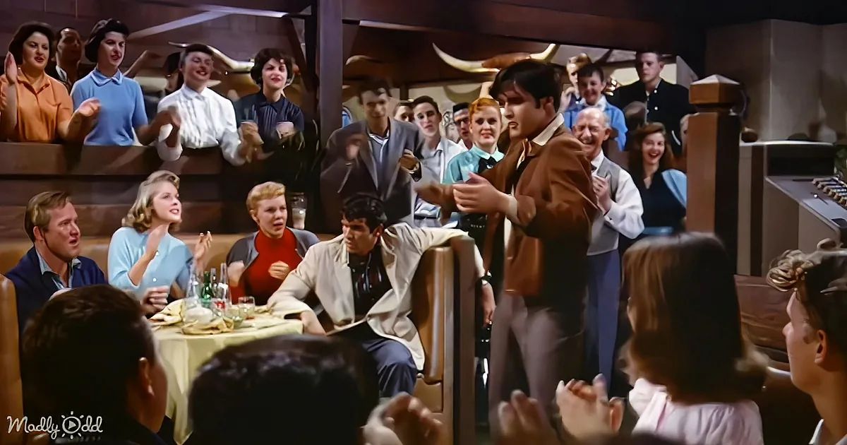 Elvis Presley dances energetically in a crowded, lively restaurant, captivating the audience with his performance.