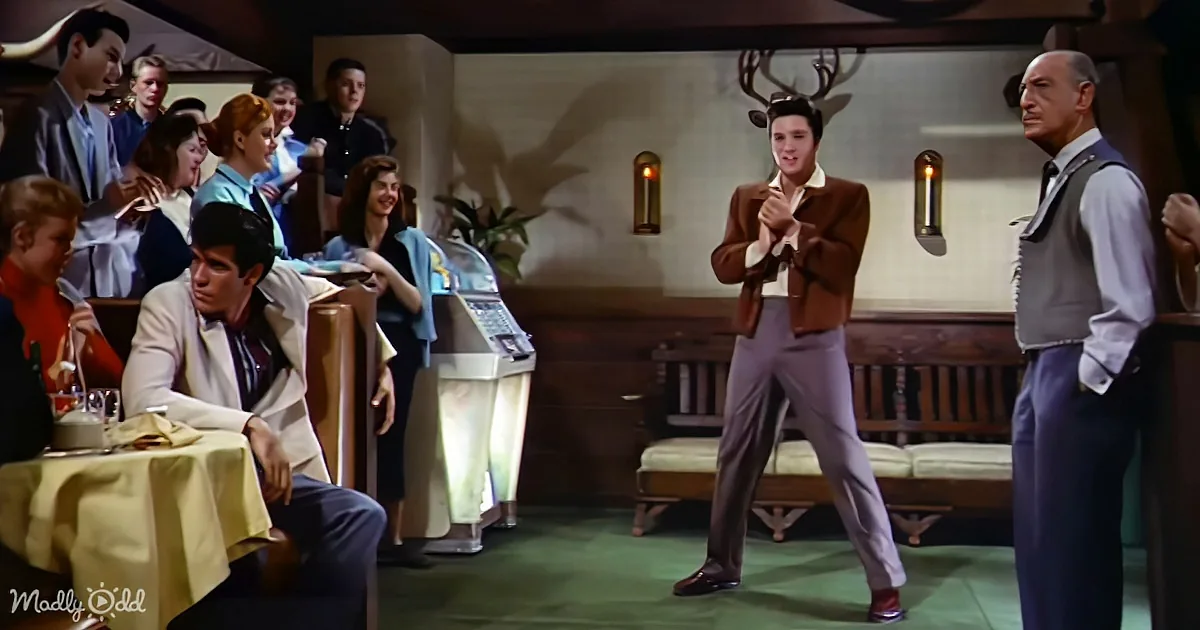 Elvis Presley dances in a restaurant, surrounded by patrons and a jukebox.