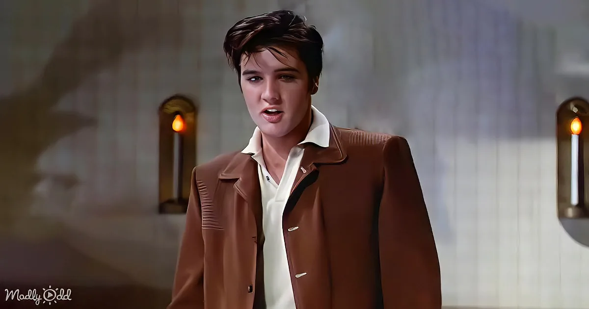 A person in a brown jacket and white shirt stands in a dimly lit room with candles.